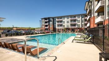 A swimming pool with sun loungers and apartment buildings in the background.