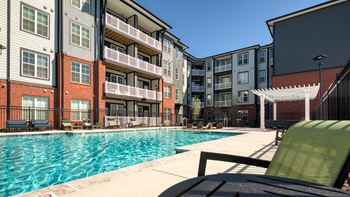 A pool area with a chair and umbrella in front of apartment buildings.