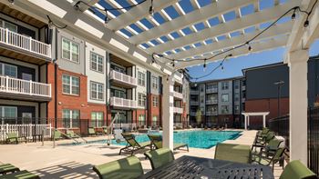 A pool area with a white pergola and green lounge chairs.