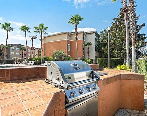 A grill is on a patio with a building and palm trees in the background.