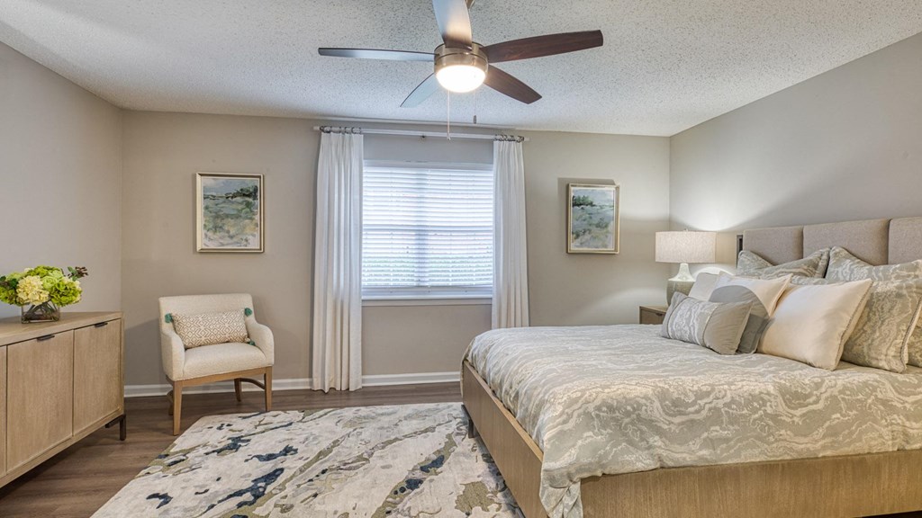 A bedroom with a bed, chair, and a ceiling fan.