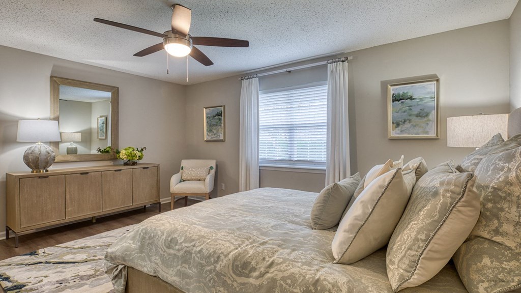 A bedroom with a large bed, a ceiling fan, and a chair.
