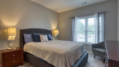 A bedroom with a large bed, a chair, and two lamps.