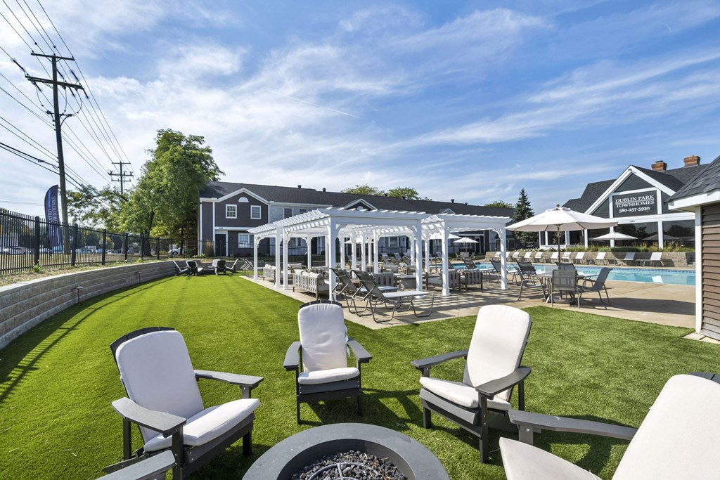 A lawn with chairs and a pool in the background.