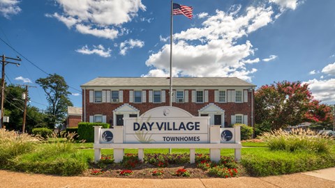 A sign for Day Village Townhomes stands in front of a brick building.