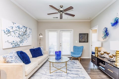 A living room with a beige couch, a blue chair, and a painting on the wall.