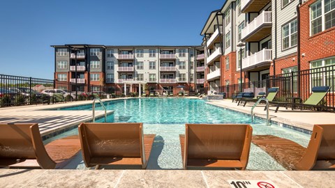 A pool with chairs and a building in the background.