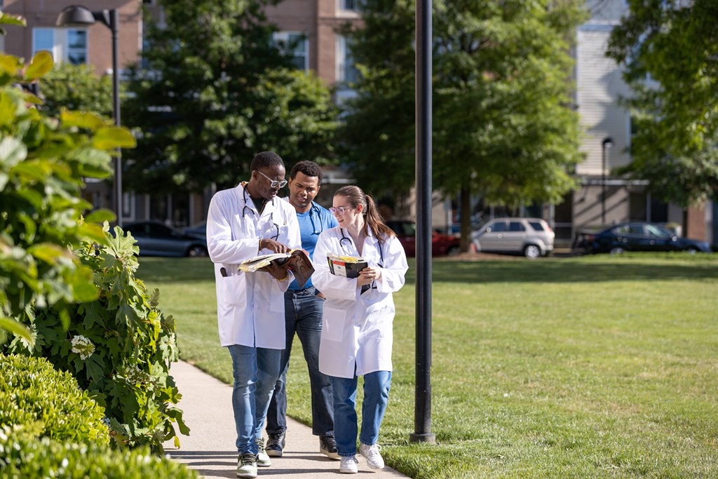 three people in white lab coats walking on a sidewalk