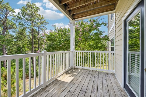 A wooden deck with a white railing and a view of trees.