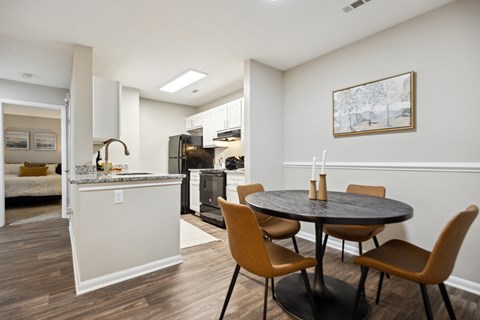 A kitchen with a table and chairs in the foreground and a microwave and oven in the background.