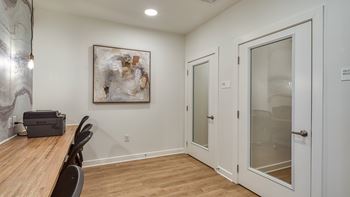 A room with a wooden table and chairs, a painting on the wall, and a door with a glass panel.