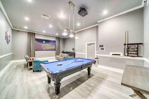 A pool table is in the middle of a room with a television and a bar.