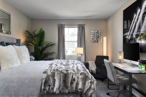 A bedroom with a large bed, a desk with a computer, and a chair.