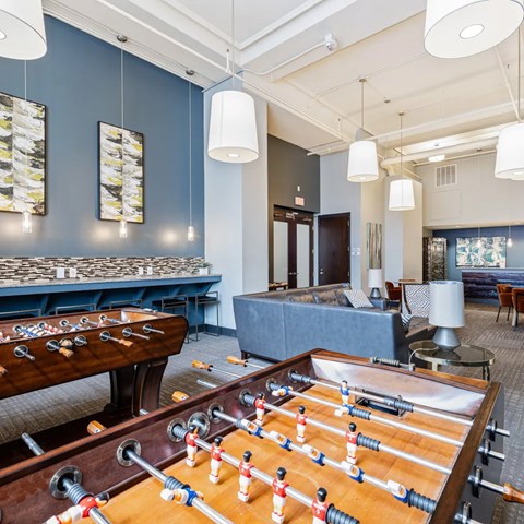 A foosball table is in the middle of a room with a pool table and couches.