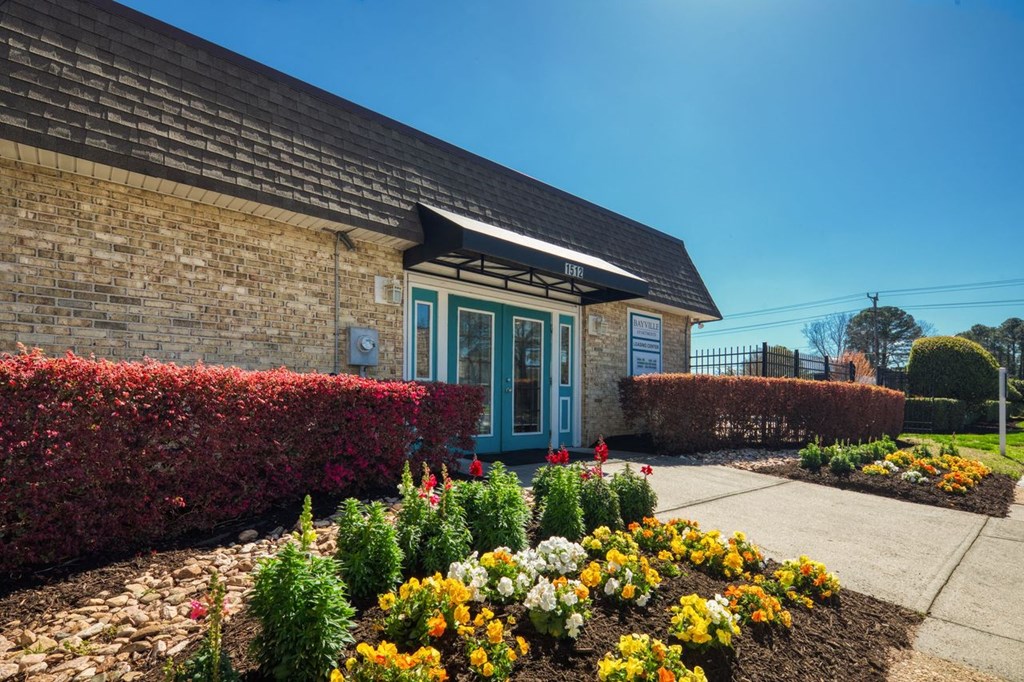 the front of a brick building with a flower garden  at Bayville Apartments, Virginia, 23455