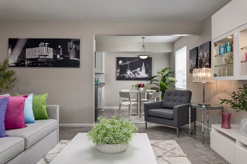 A living room with a grey couch, a black chair, a white coffee table, and a black and white photograph on the wall.