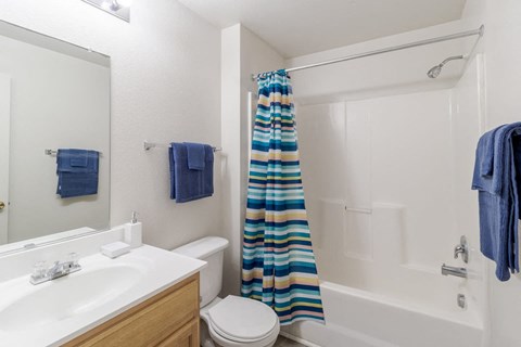 A white bathroom with a blue towel and a striped shower curtain.