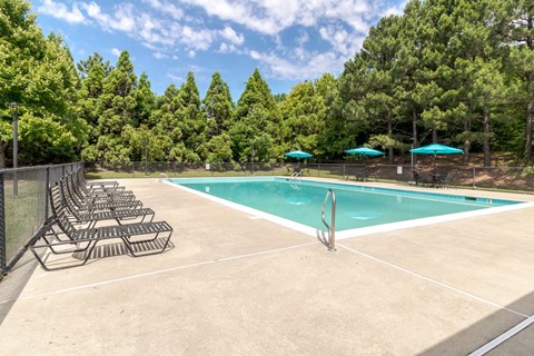 A pool surrounded by trees and lounge chairs.