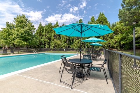 A pool area with a table and chairs and a blue umbrella.