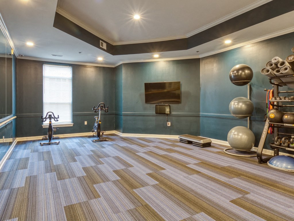 a gym with a tv and weights in a room with a wooden floor