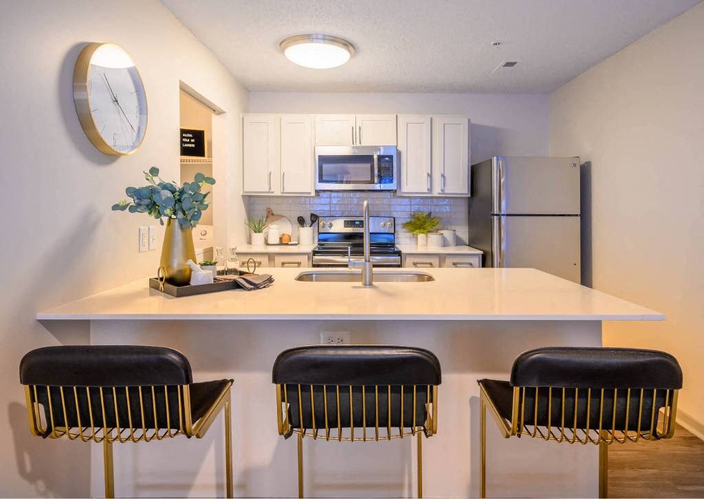 A kitchen with white countertops and black barstools.