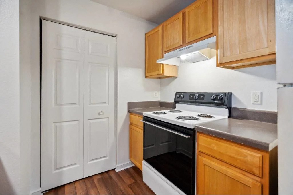 A kitchen with a white door, wooden cabinets, and a black stove top oven.