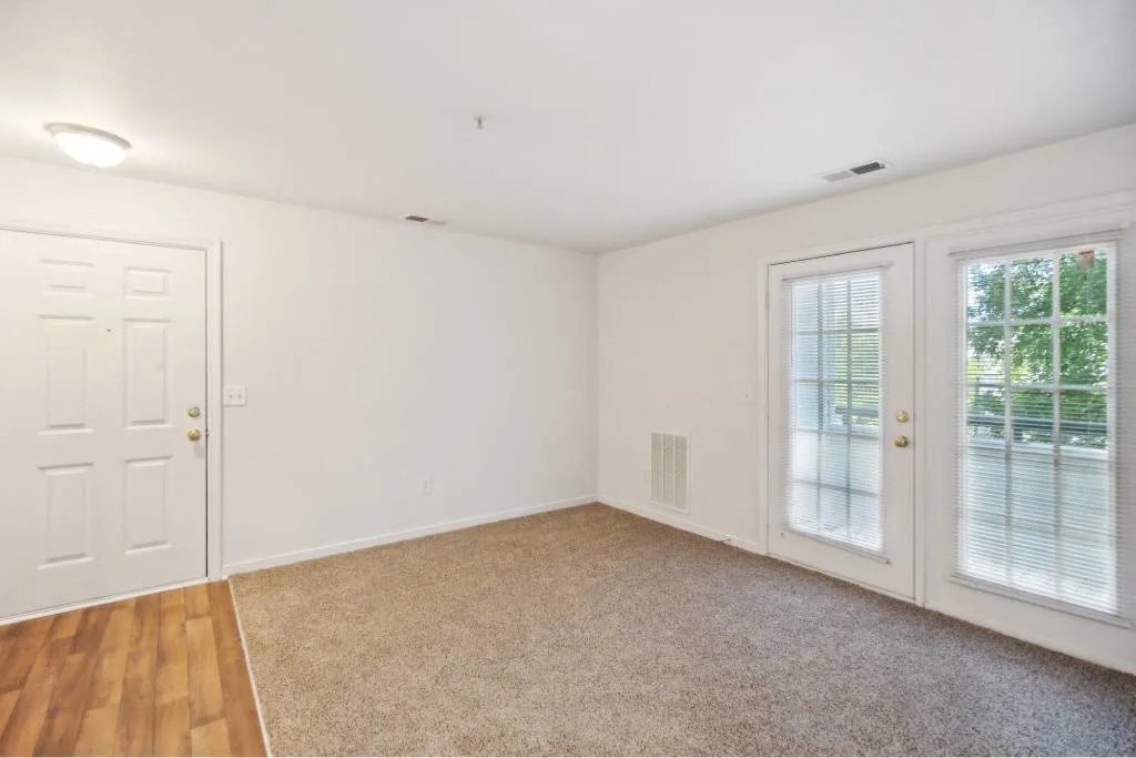 A room with a white door, carpeted floor, and a window with blinds.