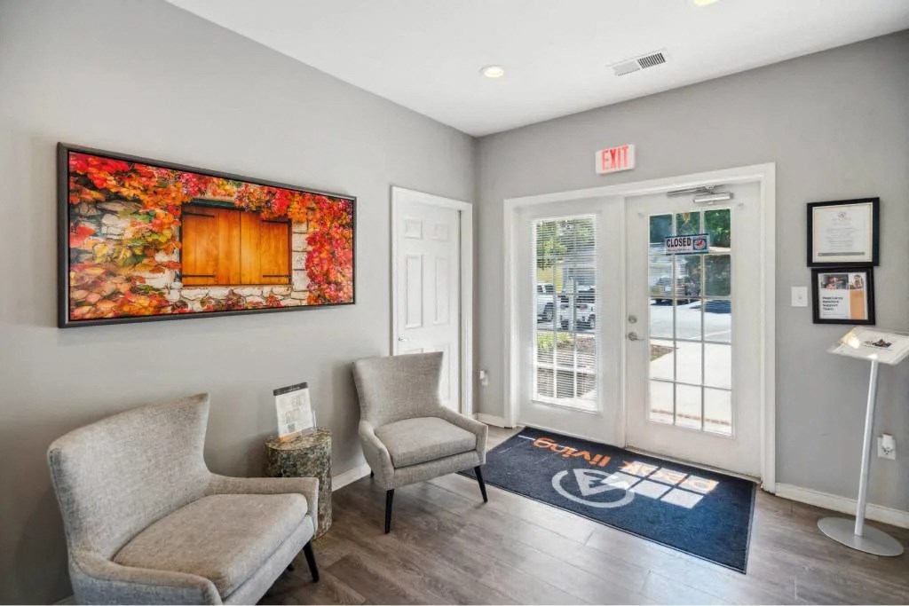 A room with a grey sofa, a chair and a painting on the wall.