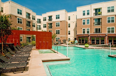A swimming pool in front of a building with a red wall.