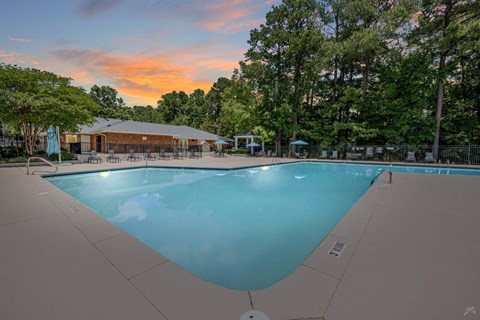 A large swimming pool surrounded by trees and a building in the background.