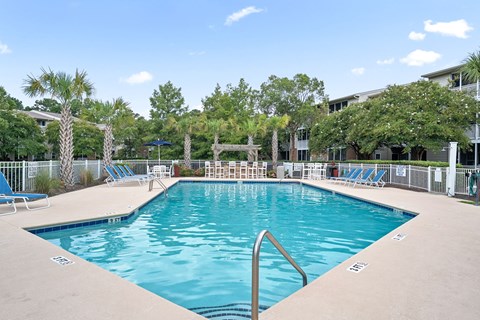A large swimming pool surrounded by palm trees and lounge chairs at Litchfield Oaks Apartments in Pawleys Island, 29585