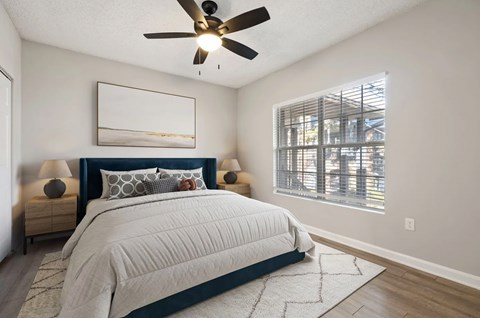 A bedroom with a large bed, a ceiling fan, and a window with blinds.