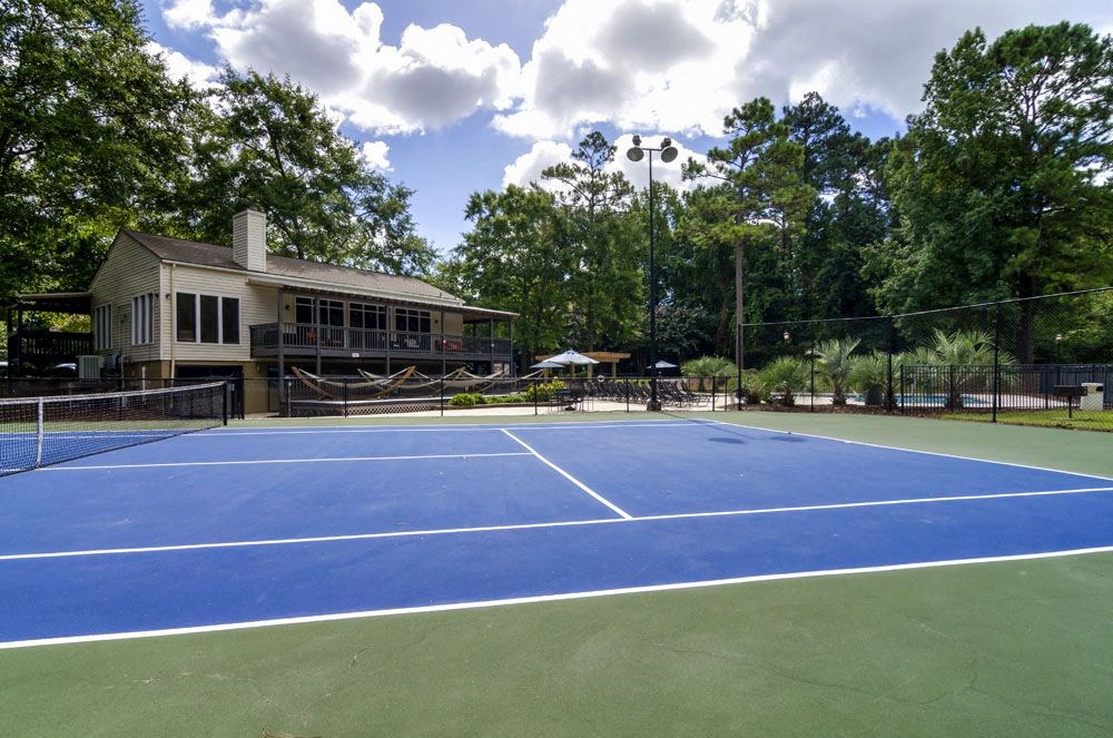 a blue tennis court with a house in the background