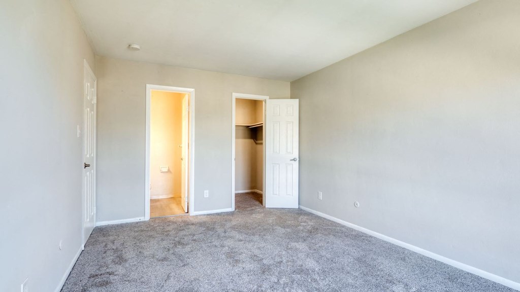 an empty living room with carpet and a door to a closet at Bayville Apartments, Virginia Beach, VA