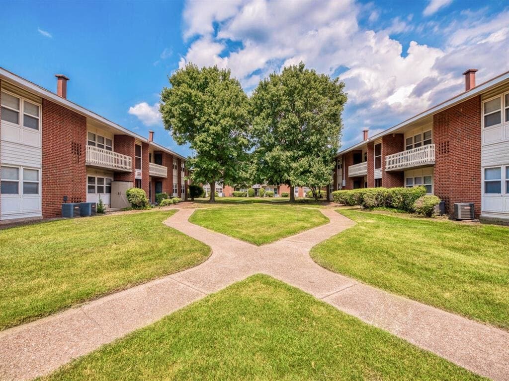 a courtyard between two apartment buildings with grass and trees at Gates of West Bay, Norfolk, VA