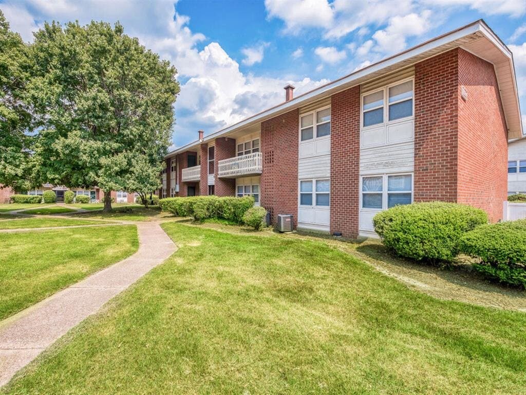 a brick apartment building with a sidewalk and green grass at Gates of West Bay, Norfolk, 23503