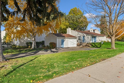 A house with a grey roof and a white garage door is surrounded by trees with yellow leaves.