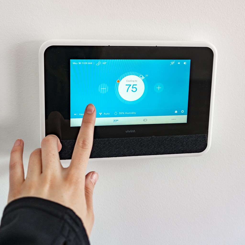A person is pointing at a Vivint thermostat displaying 75 degrees.