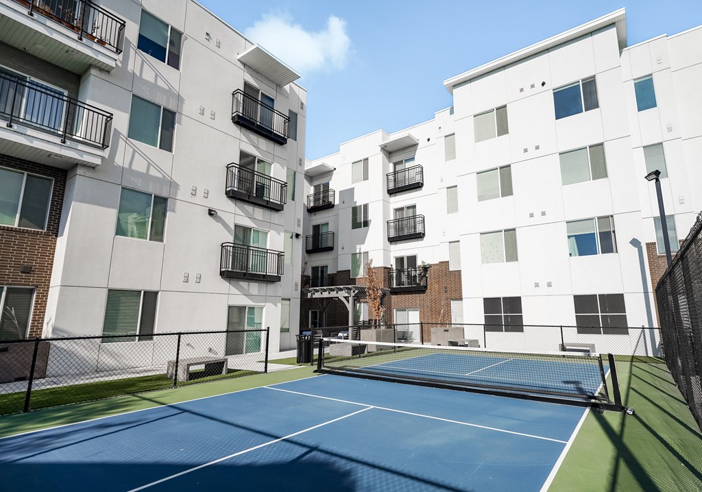A tennis court is located in front of a white apartment building.