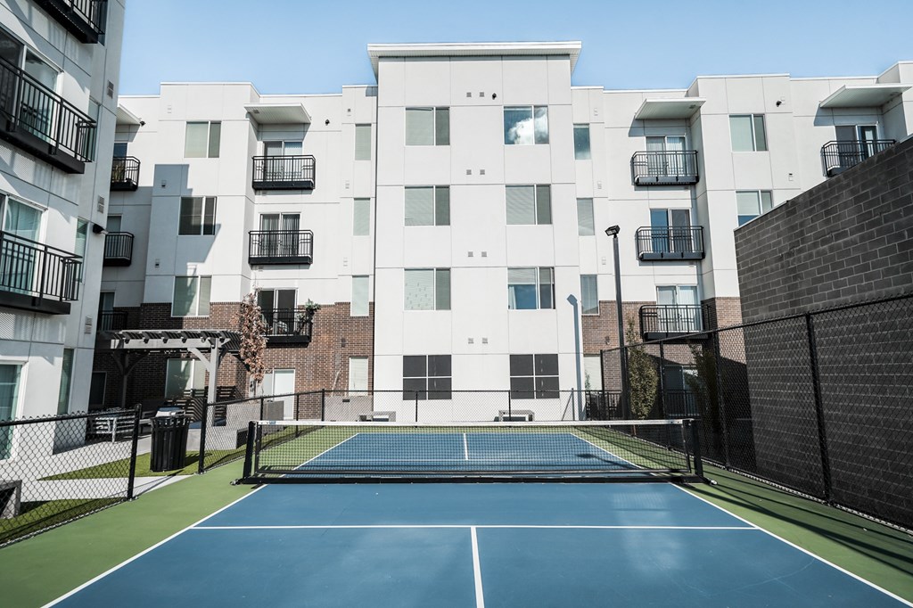 A tennis court is located in front of a white apartment building.