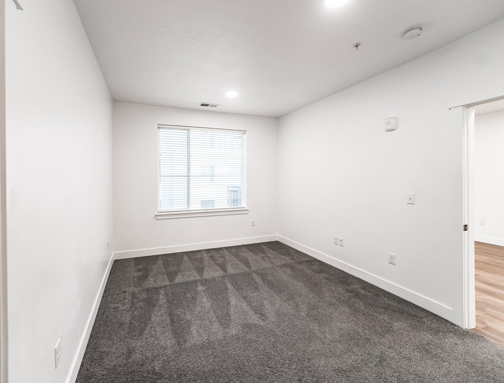 A room with a carpeted floor and a window with blinds.