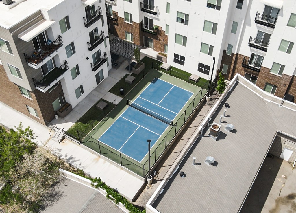 A tennis court is surrounded by apartment buildings.