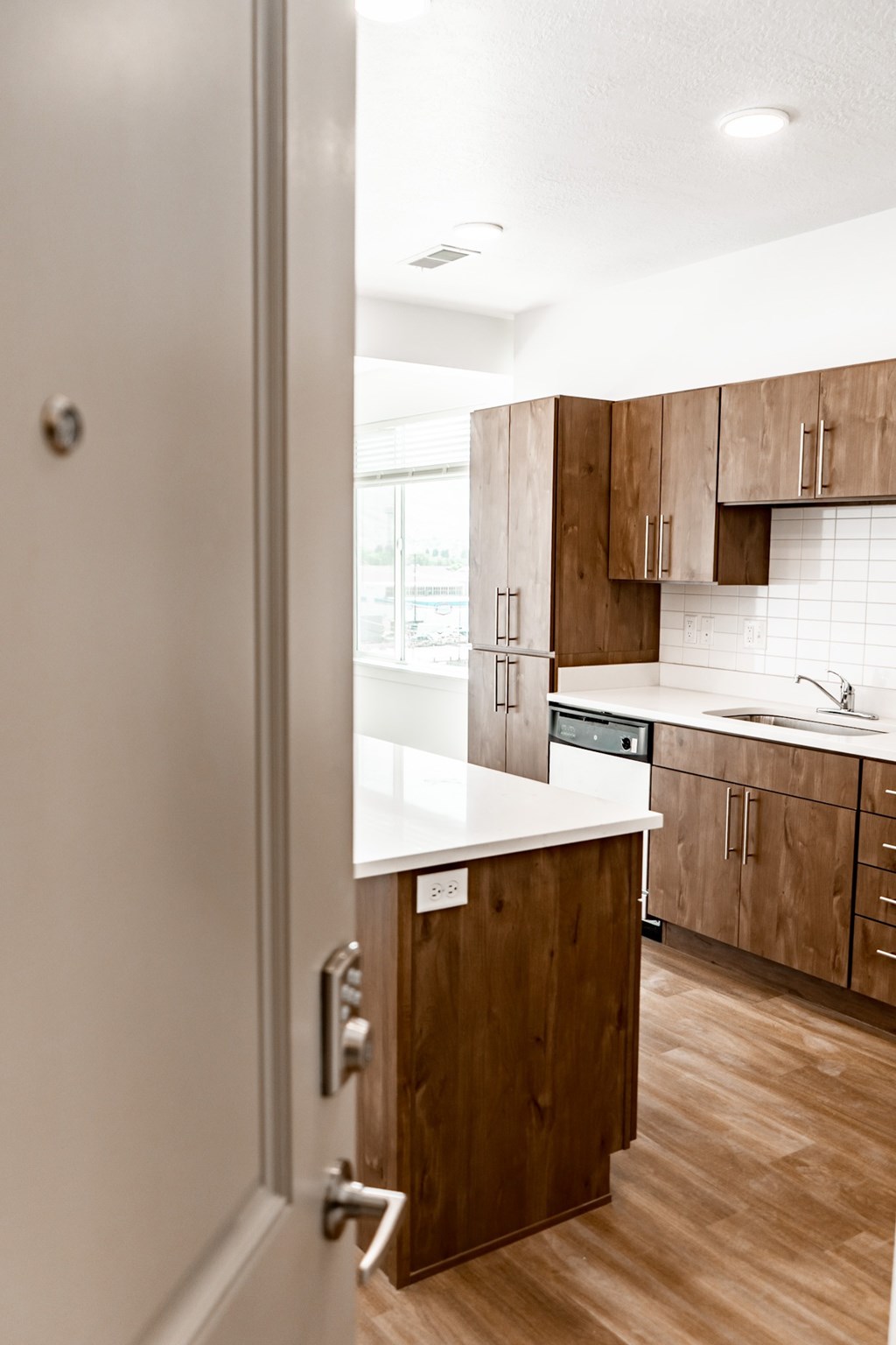 A white door opens to a modern kitchen with wooden cabinets.