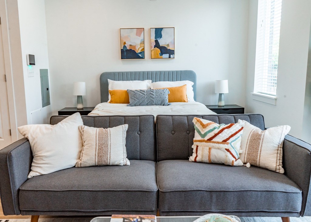 A grey couch with a grey headboard and pillows in front of a bed.