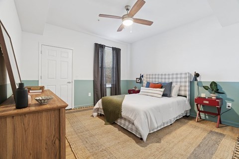 A bedroom with a bed, nightstand, and a fan.