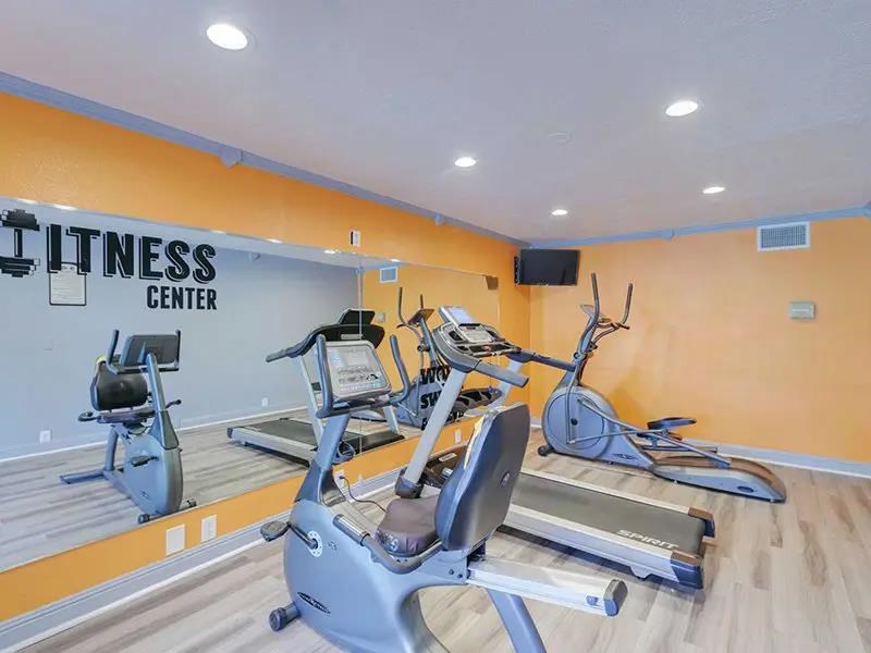 A fitness center with a row of treadmilers and a television mounted on the wall.