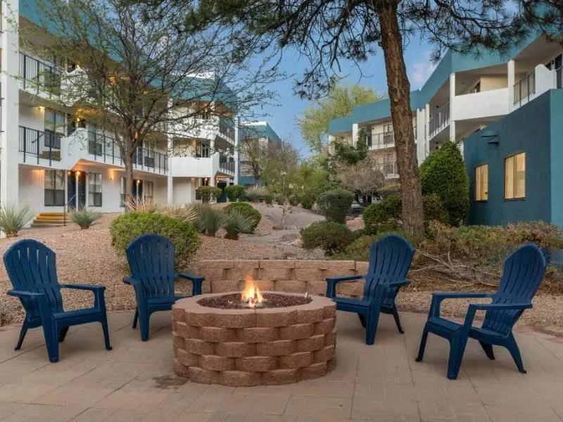 A fire pit surrounded by blue chairs in front of apartment buildings.