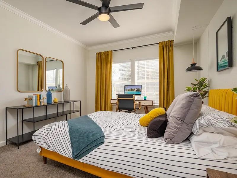 A bedroom with a bed, a desk, a mirror, and a ceiling fan.