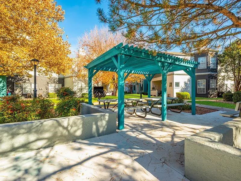 A green gazebo with a table and chairs is surrounded by trees with yellow leaves.