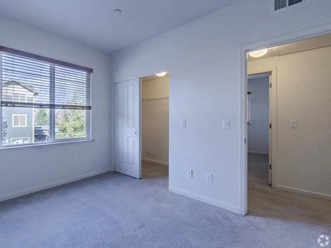 A spacious room with a window, carpeted floor, and two doors.